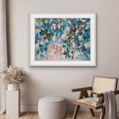 An original painting on canvas of a leafy canopy scene in soft calm grey green, mint and peach tones in a bespoke off white frame. Set against a soft blush wall with wicker chair and beige pouf