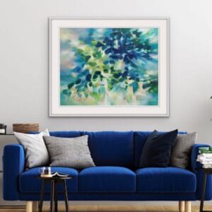 An original painting on canvas in Soft Green and Blue colours with pops of yellow, of a leafy tree canopy with a Spring like feel in a bespoke with frame. set against a light white wall over a blue velvet sofa.