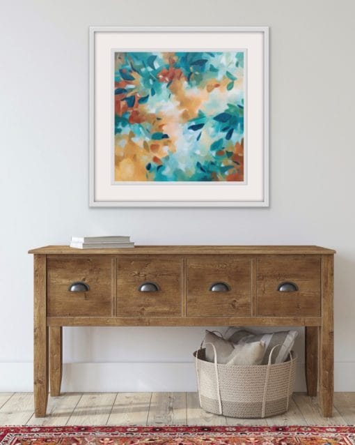 An original painting on canvas of a leafy canopy scene in mellow autumnal rust and pine green shades, in a bespoke off white frame. Set against an off white wall over a sideboard with drawers and basket.