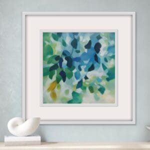 An original painting on canvas of tree leaves in spring like shades of blue and green, with a hint of yellow, in a bespoke off white frame set against a soft grey wall with a console table below.